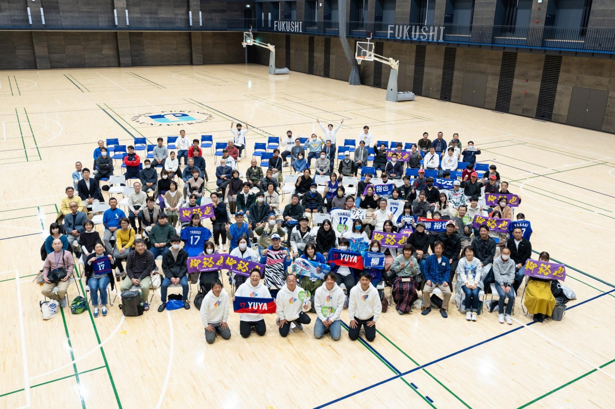体育館内で選手のユニフォームやタオルを掲げ、参加者120名程の集合写真